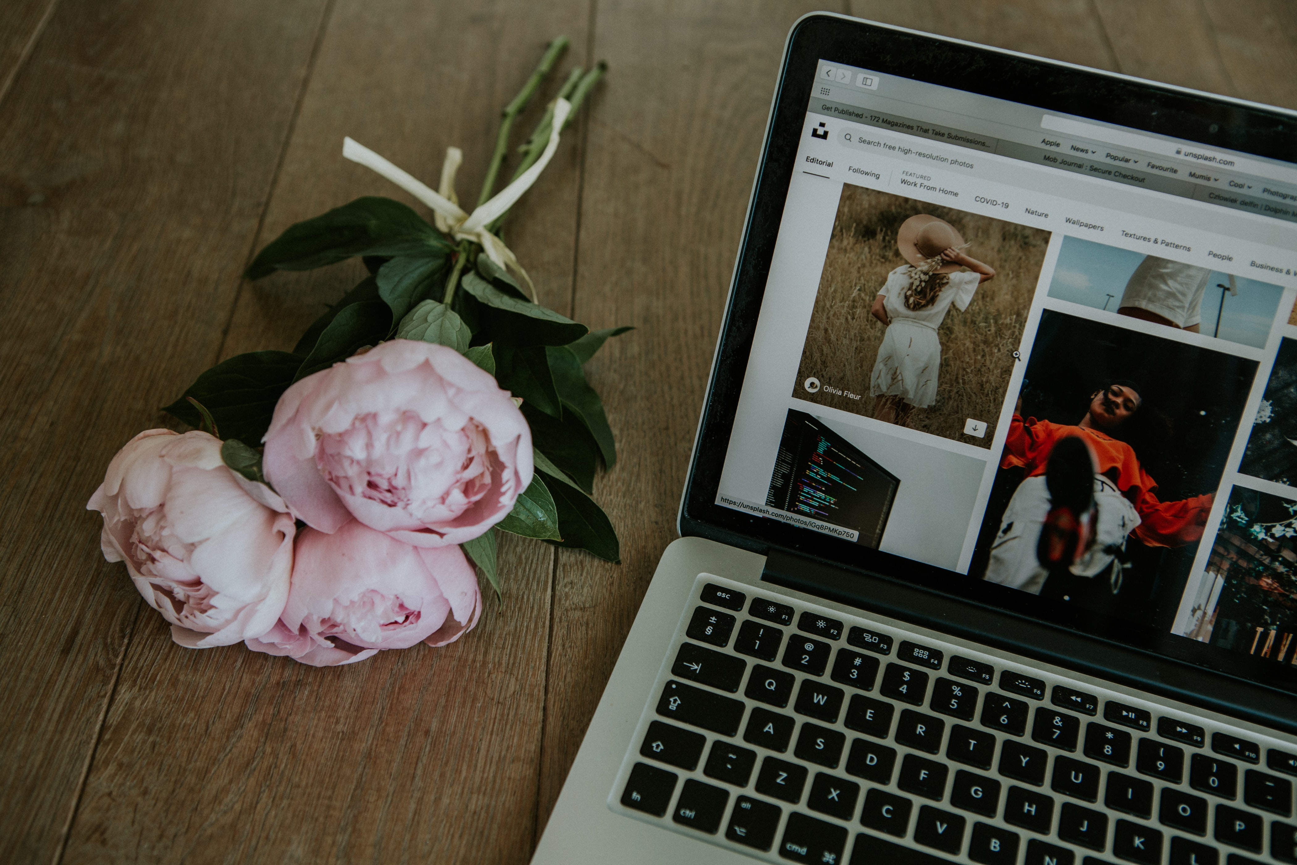 Image of a laptop on a wooden surface next to a bundle of white flowers displaying a web page.